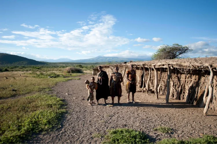 Group of East African locals smiles gleefully for a picture with a wide open field in the background.