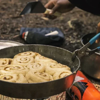 A student cooks cinnamon rolls in a fry bake over a Whisperlite.