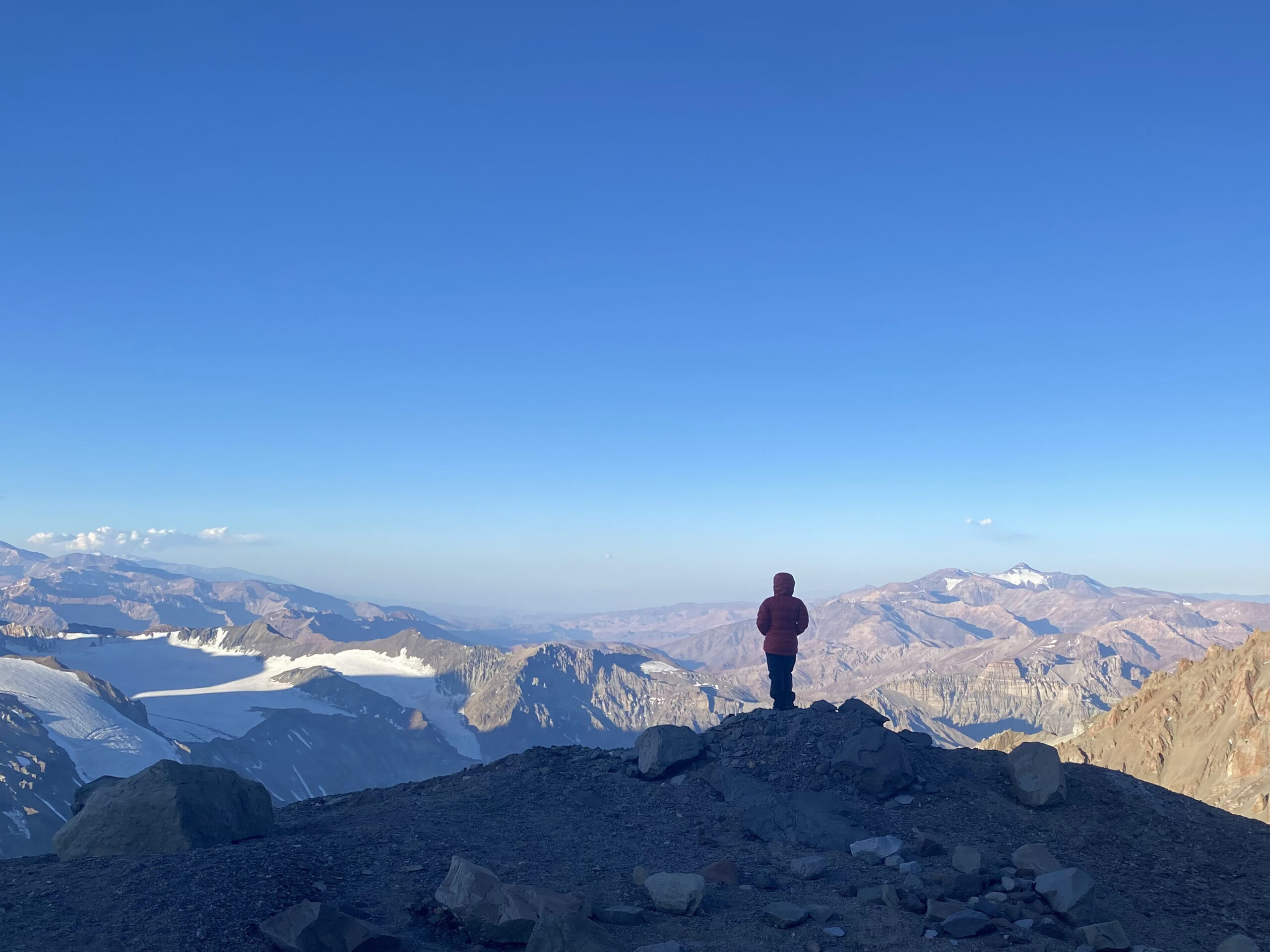 Solo person in a red parka looking out over a vast mountain range