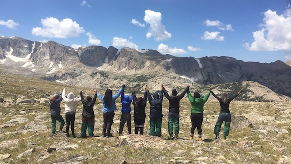 C5 students on a NOLS course in the Wind River Range hold hands with outstretched arms while looking out at the mountains