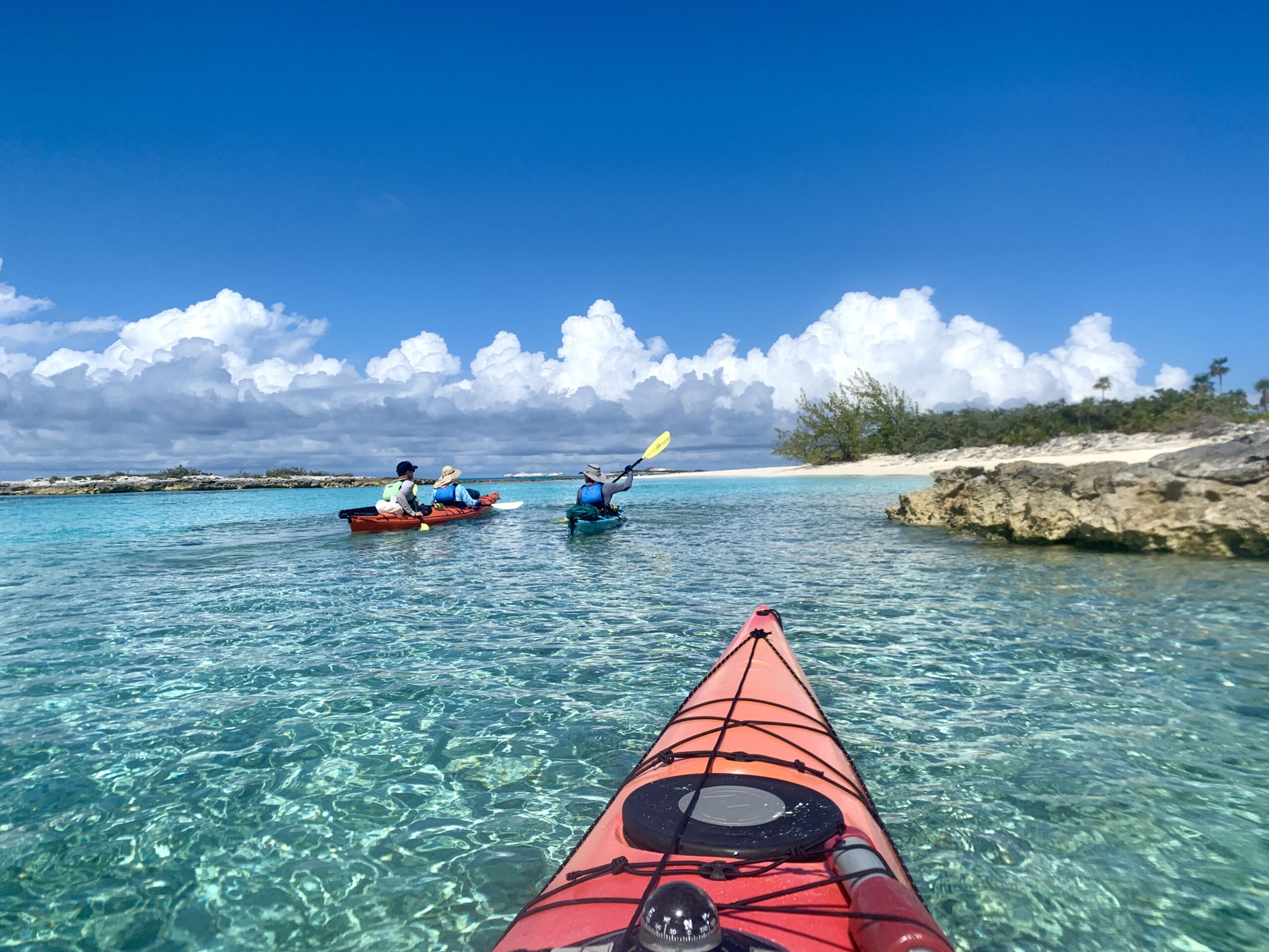 View from a kayak looking ahead to three other kayakers gliding over crystal clear water