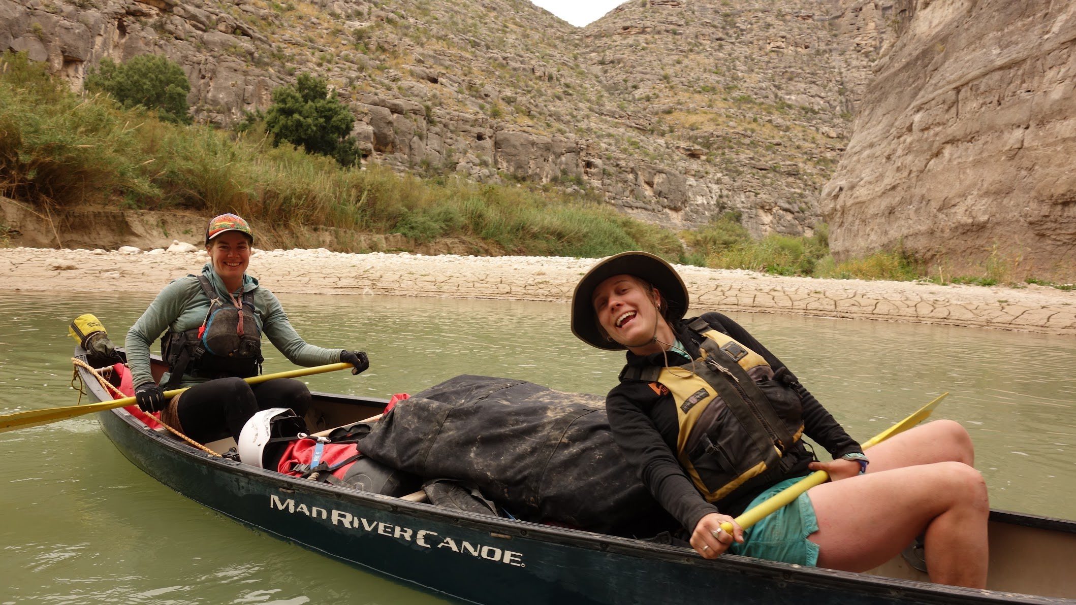 Two people smiling and paddling a canoe