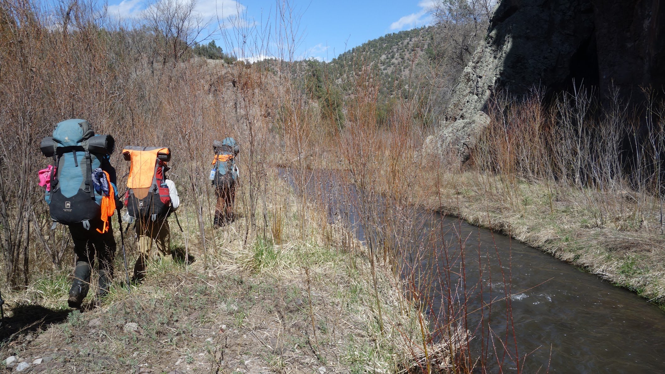 People hiking with backpacks on a riverbank