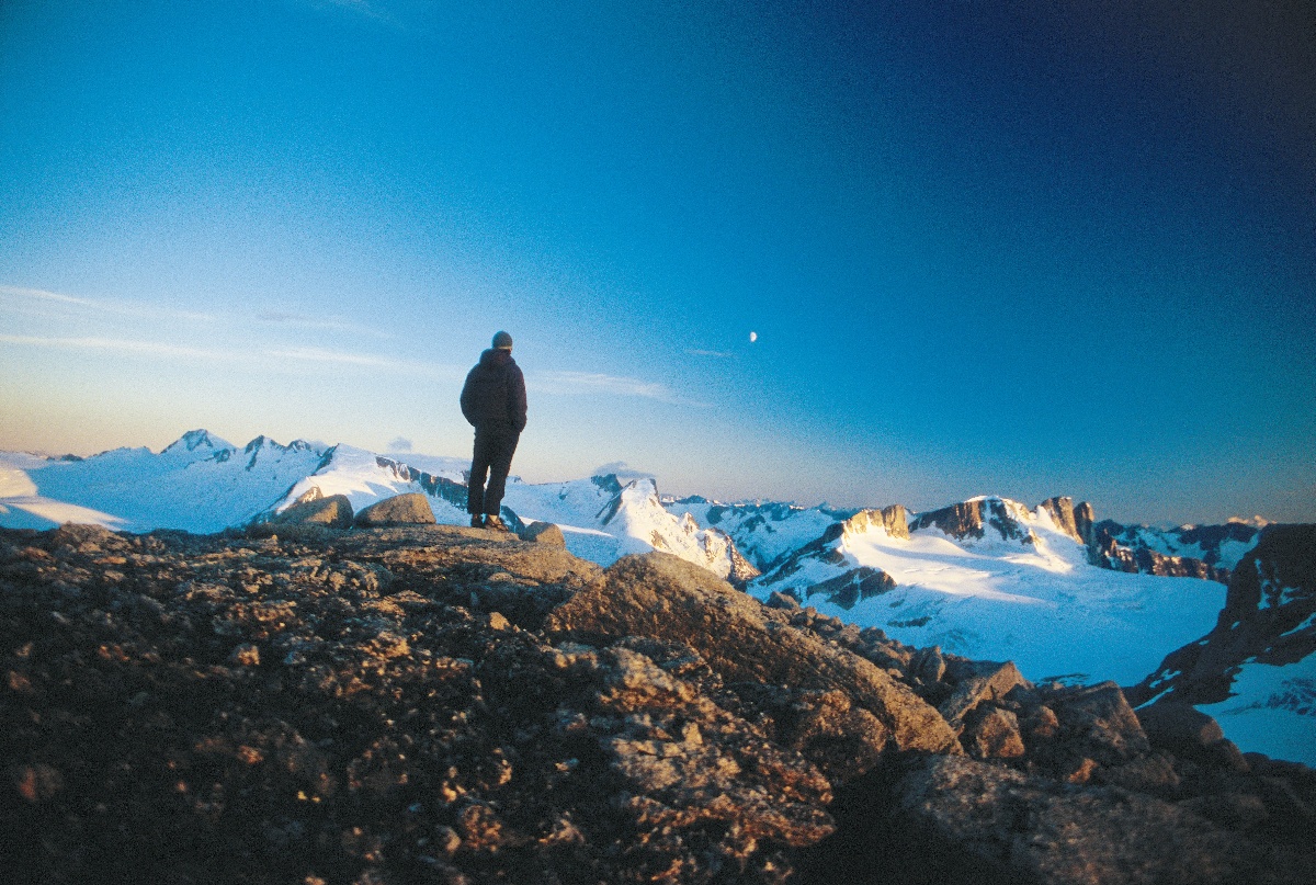 Person stands on mountaintop looking at moonrise over faraway ridges