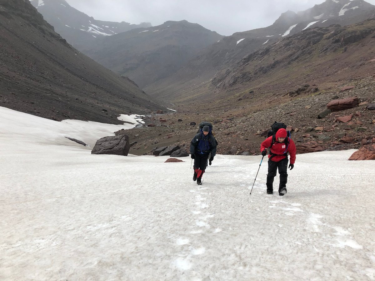 two students use trekking poles to ascend a steep snowfield