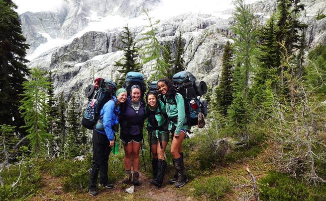 Four girls pose on a mountain slope in the Pacific Northwest while backpacking.