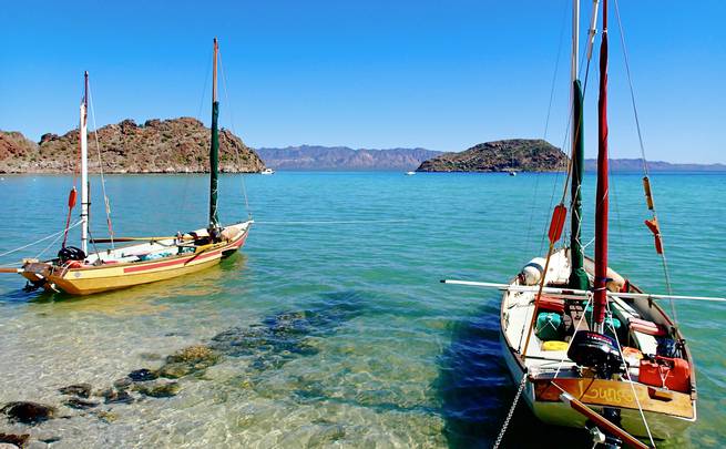 Two sailboats anchored near the shore in the bright aqua waters of Baja California, Mexico.