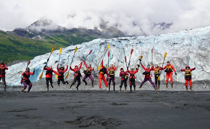 A course jumps together with their sea kayaking paddles on a beach in Alaska.