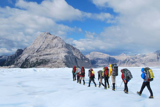 Students use crampons to backpack across a snowy field surrounded by mountains in Patagonia.