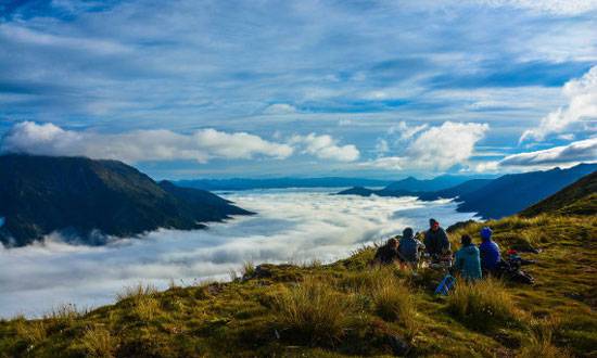 Course participants sit on a grassy ridge above the clouds in Kahurangi National Park.