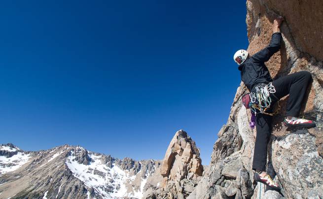 A student rock climbs near snow dusted peaks in Patagonia.