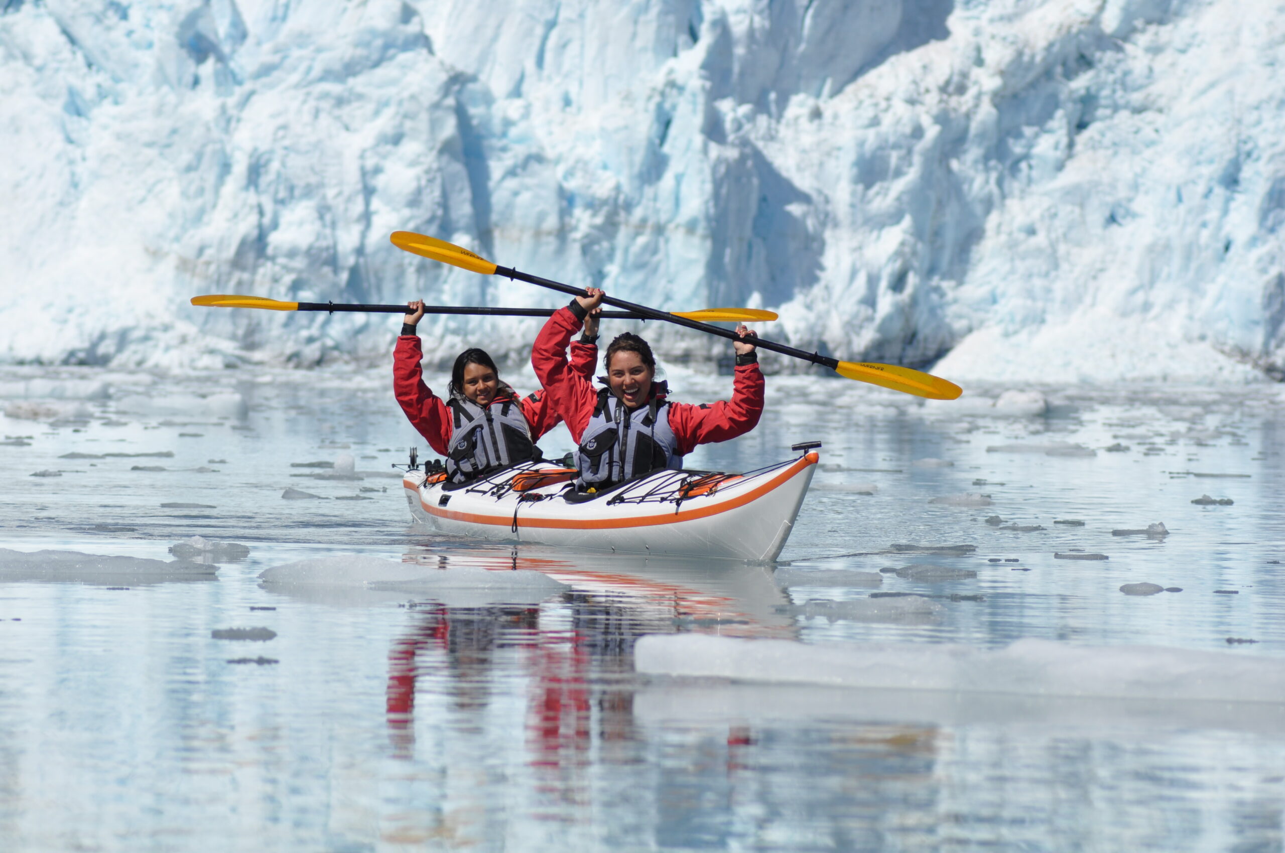students in sea kayaks pose in front of a glacier in Alaska