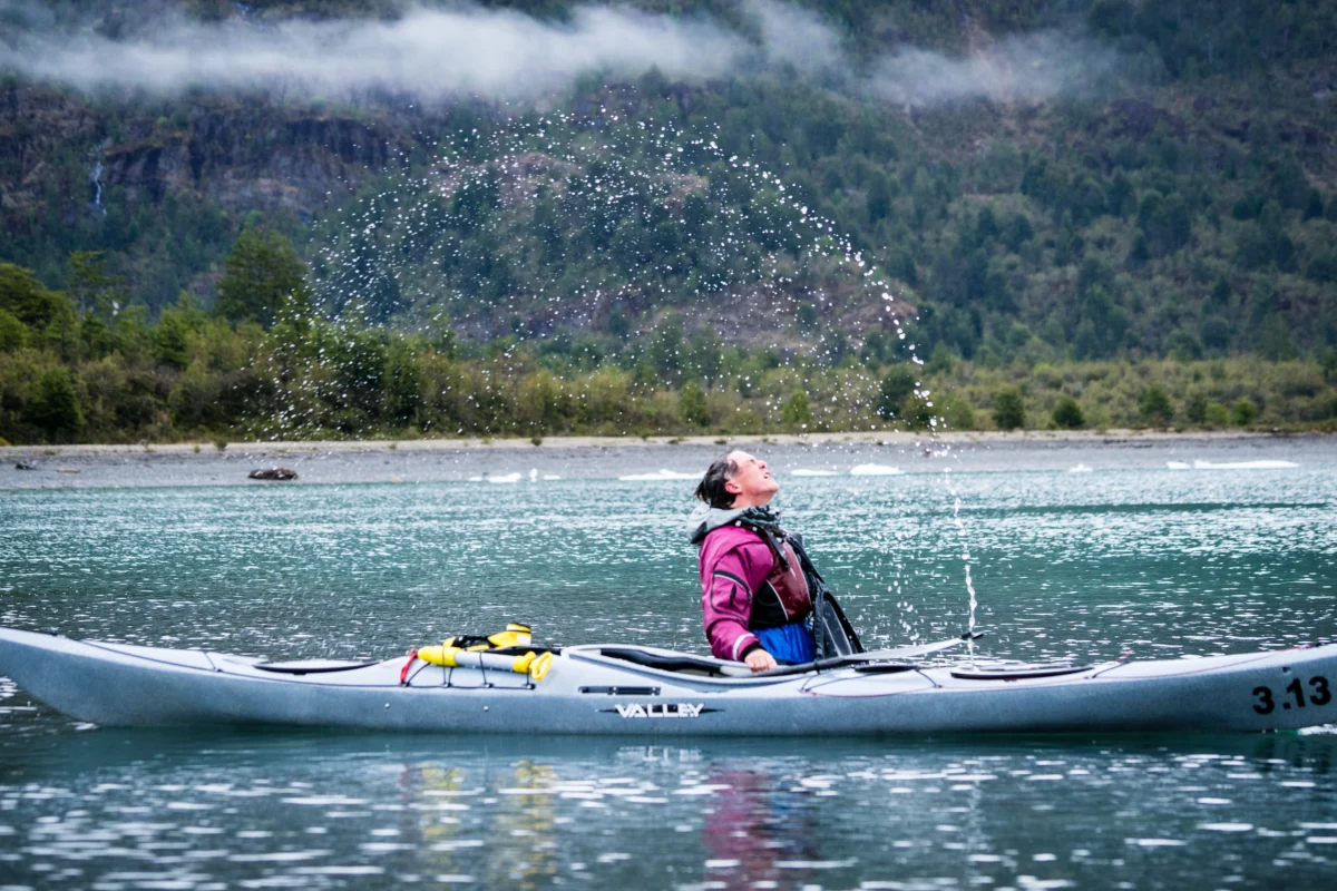 a sea kayaker in a boat flips their hair creating an arc of water drops.