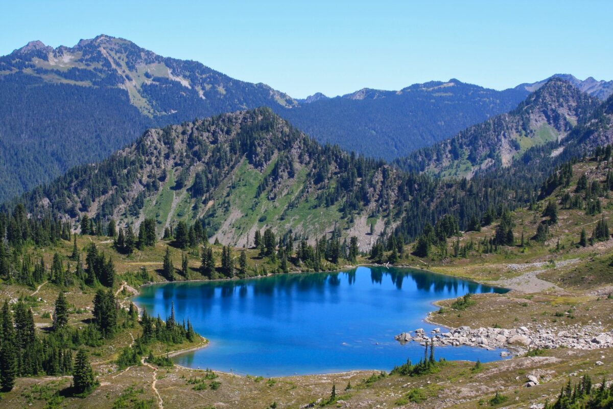 Cobalt-blue lake surrounded by mountains and evergreen trees along Seven Lakes Basin Loop in Olympic National Park.