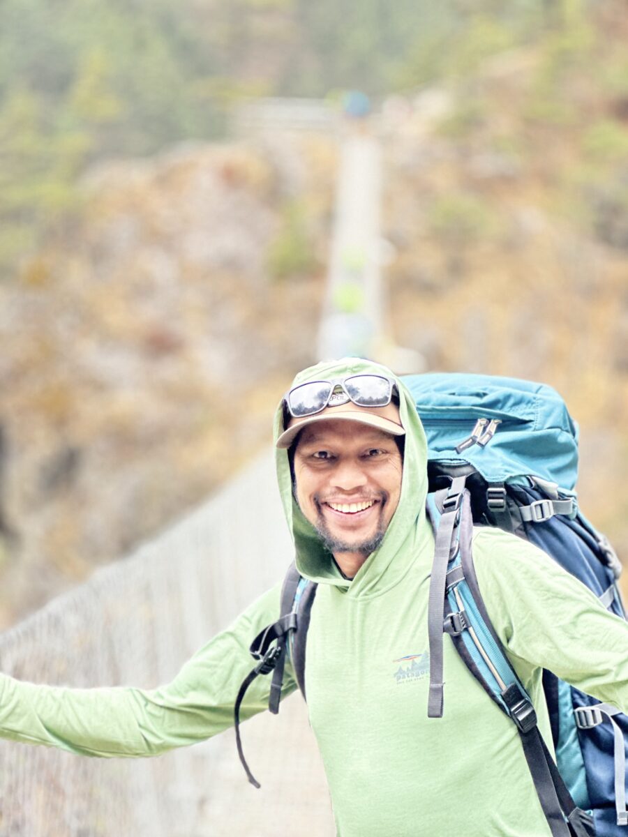 Jagan Timilsina, wearing a light green jacket and a blue backpack, photographed on a bridge.