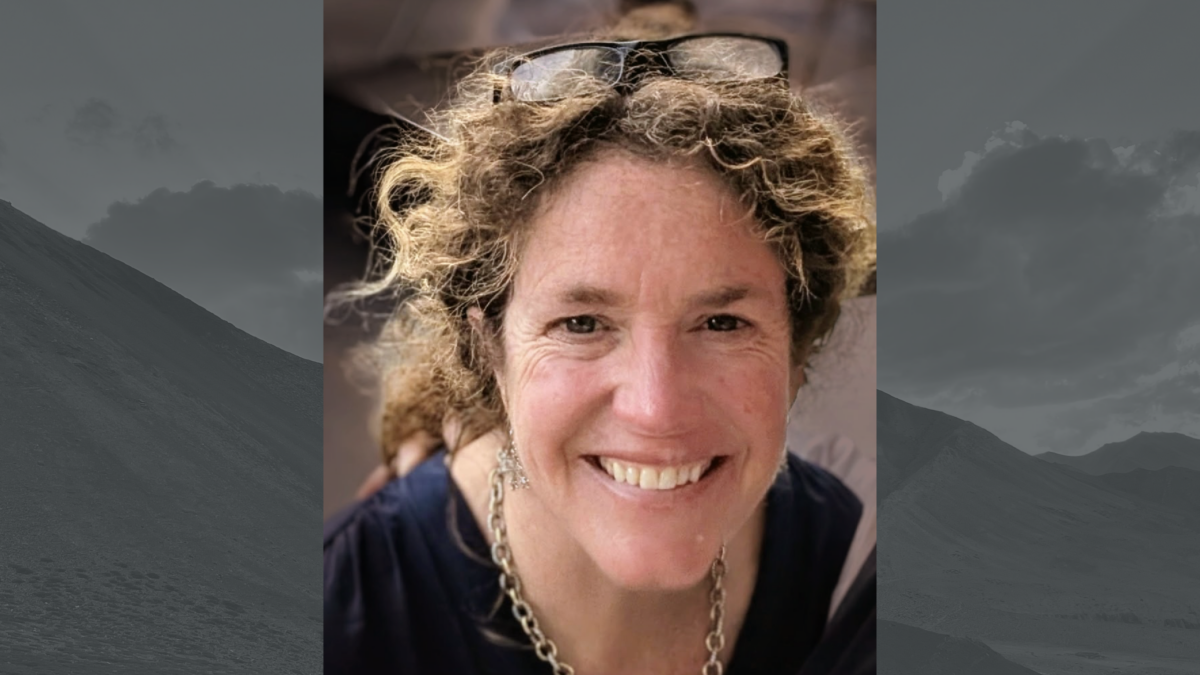 a woman with curly hair in a ponytail and glasses on her head smiles for the camera.