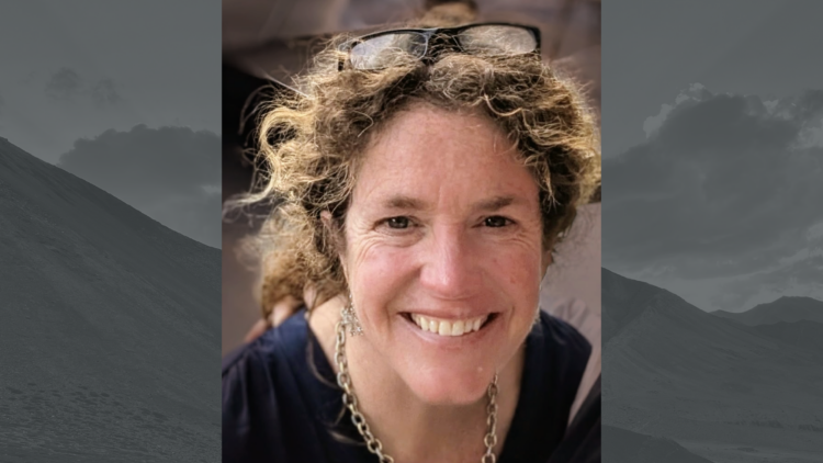 a woman with curly hair in a ponytail and glasses on her head smiles for the camera.