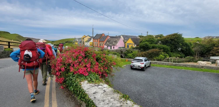 Hikers walk along the road with colorful buildings to the right