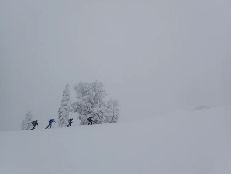 four people ski up a ridge in whiteout conditions