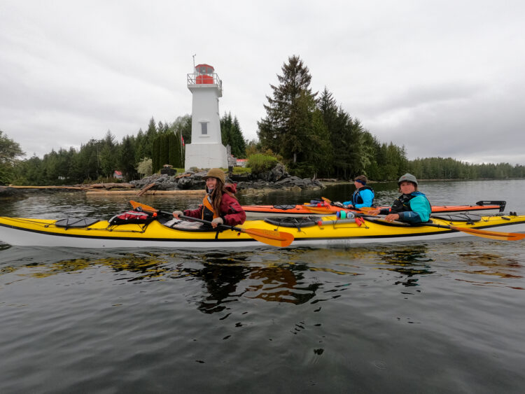 Kayakers pose with light house behind them in British Columbia
