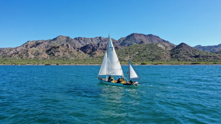 a sailboat cruises through turquoise waters. there is a mountain in the background.