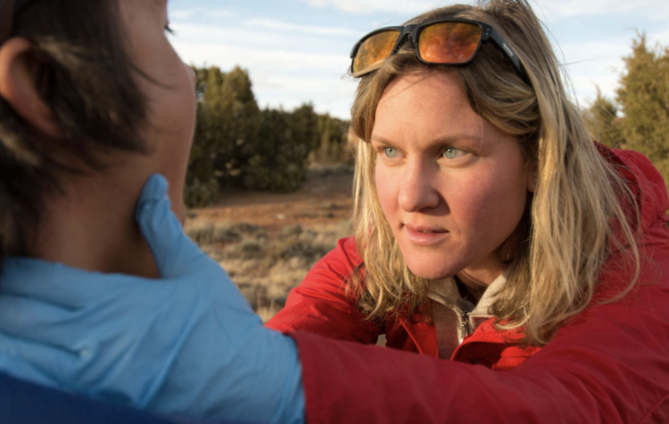 Woman in red wearing sterile gloves examines someone's fce.