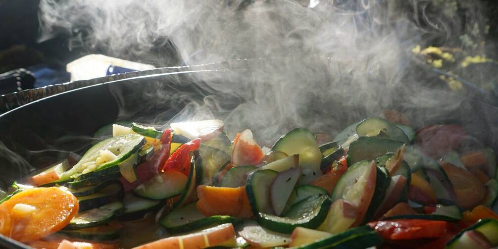 parker-woodworth-nz-20.jpg__1400x503_q70_crop_subject_location-3000,2000_subsampling-2_upscale A pot of fresh cucumbers, carrots, peppers, and other vegetables steams over a camping stove.